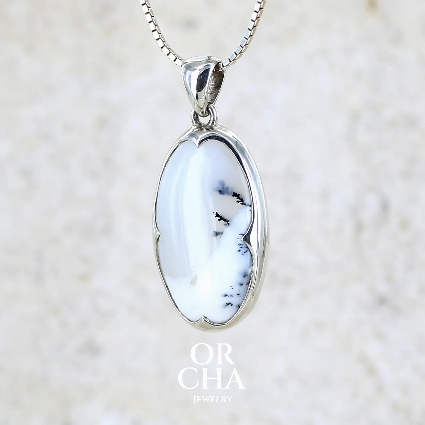 Pendentif pour femme en argent massif sertie d'un cabochon de forme ovale d'agate dendritique de couleur blanc pur et noir. Pierre opaque à translucide à inclusions paysages de dendrites de manganèse noires contrastées. Bijou unique réalisé par Orchajewelry
