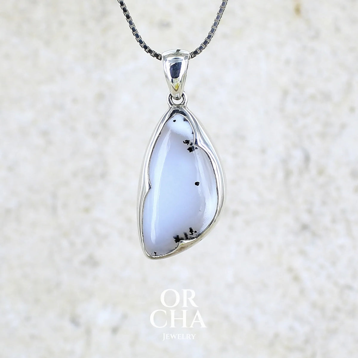 Pendentif pour femme en argent massif sertie d'un cabochon en forme d'aile d'agate dendritique de couleur blanc pur et noir. Pierre opaque à translucide à inclusions paysages de dendrites de manganèse noires contrastées. Bijou unique réalisé par Orchajewelry