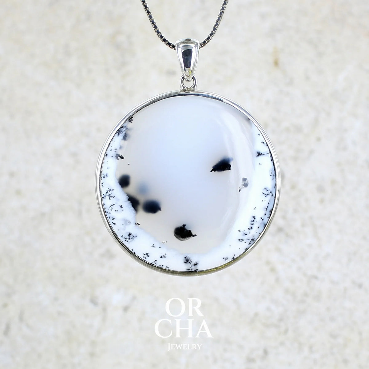 Pendentif pour femme en argent massif sertie d'un cabochon rond d'agate dendritique de couleur blanc pur et noir. Pierre opaque à translucide à inclusions paysages de dendrites de manganèse noires contrastées. Bijou unique réalisé par Orchajewelry