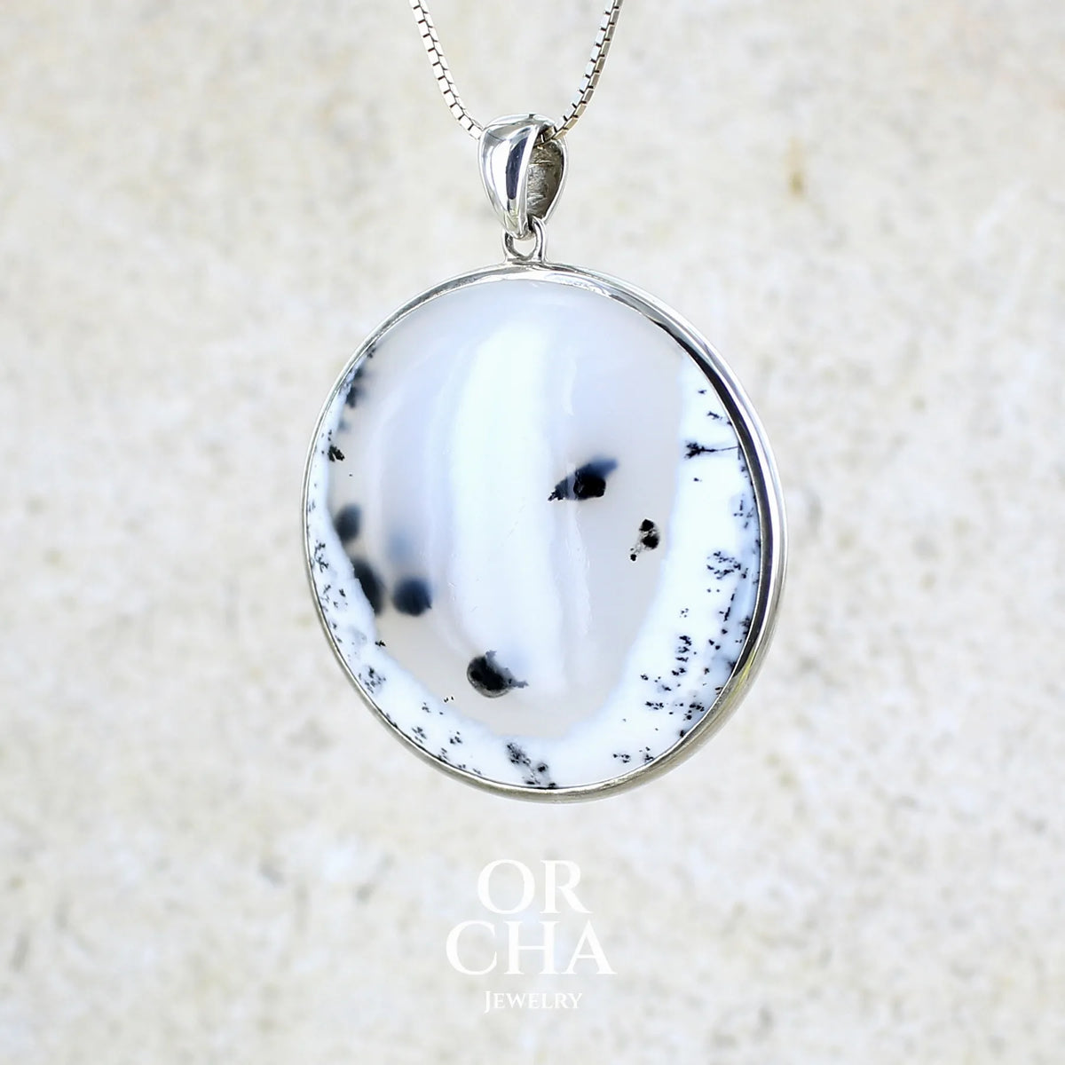 Pendentif pour femme en argent massif sertie d'un cabochon rond d'agate dendritique de couleur blanc pur et noir. Pierre opaque à translucide à inclusions paysages de dendrites de manganèse noires contrastées. Bijou unique réalisé par Orchajewelry