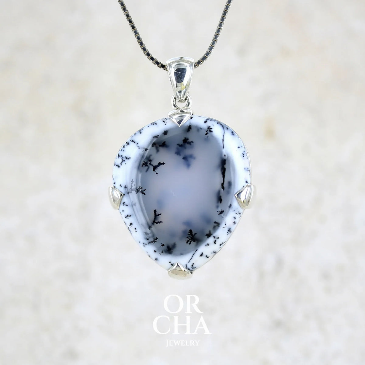 Pendentif pour femme en argent massif sertie d'un cabochon en forme de goutte inversée d'agate dendritique de couleur blanc pur et noir. Pierre opaque à translucide à inclusions paysages de dendrites de manganèse noires contrastées. Bijou unique réalisée par Orchajewelry