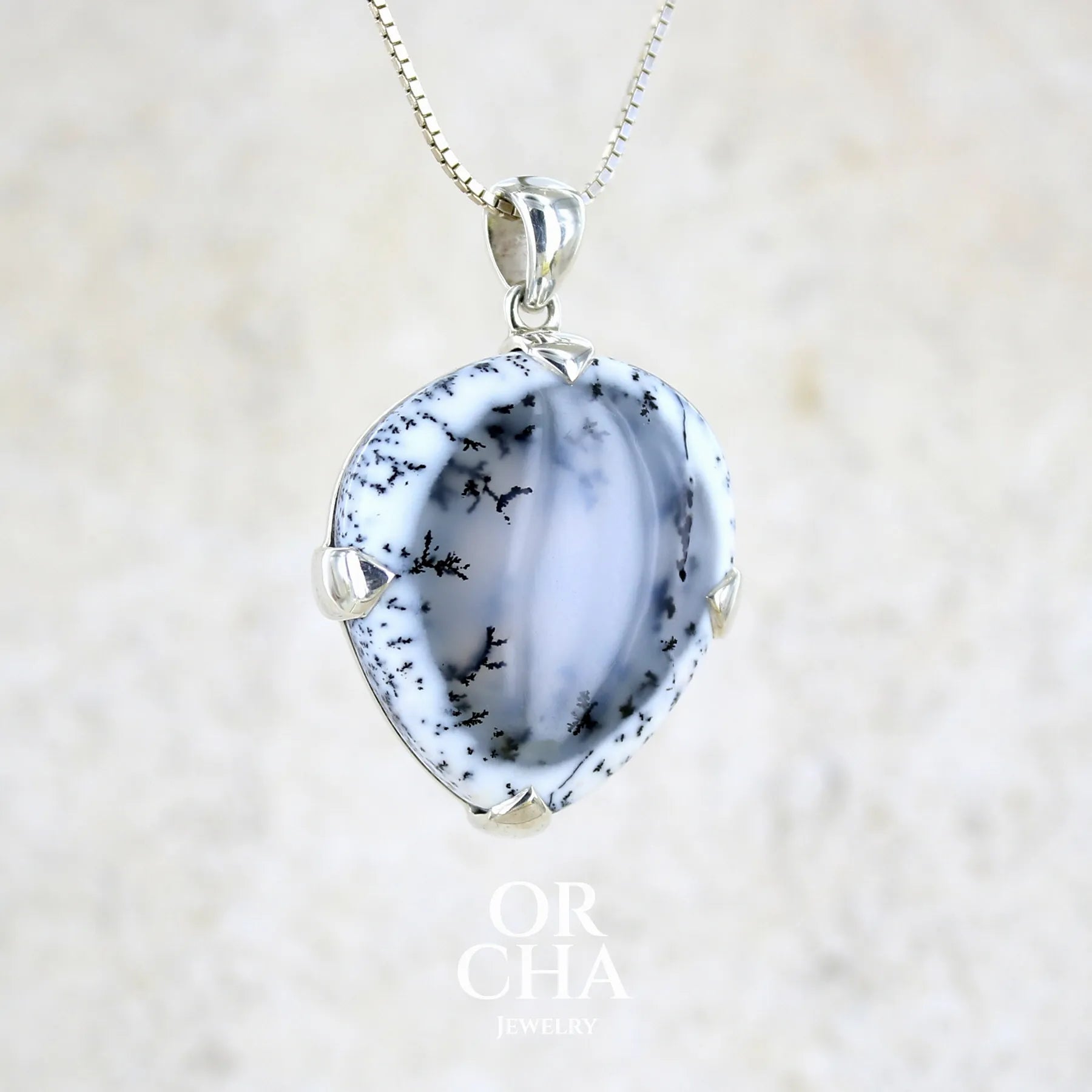 Pendentif pour femme en argent massif sertie d'un cabochon en forme de goutte inversée d'agate dendritique de couleur blanc pur et noir. Pierre opaque à translucide à inclusions paysages de dendrites de manganèse noires contrastées. Bijou unique réalisée par Orchajewelry