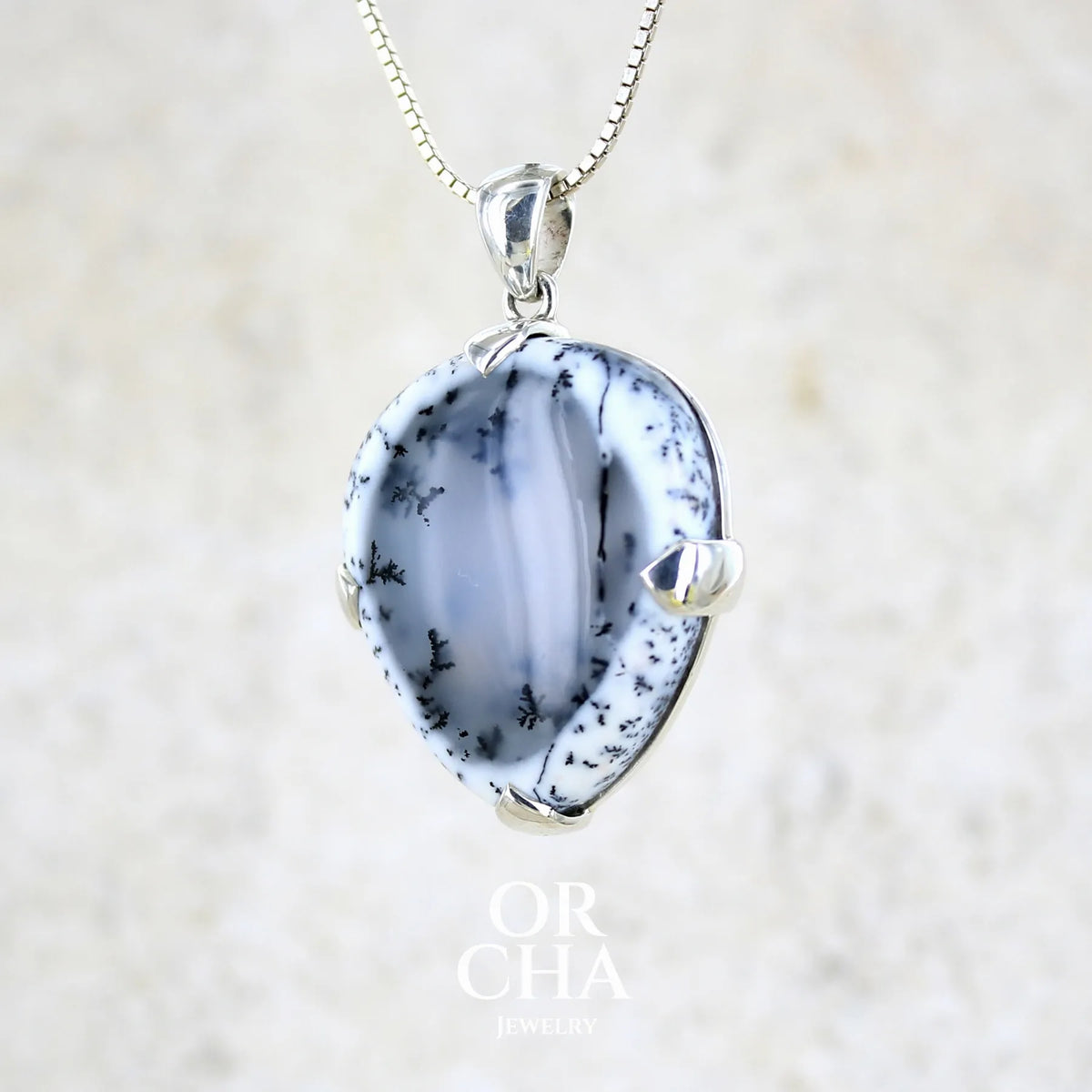 Pendentif pour femme en argent massif sertie d'un cabochon en forme de goutte inversée d'agate dendritique de couleur blanc pur et noir. Pierre opaque à translucide à inclusions paysages de dendrites de manganèse noires contrastées. Bijou unique réalisée par Orchajewelry