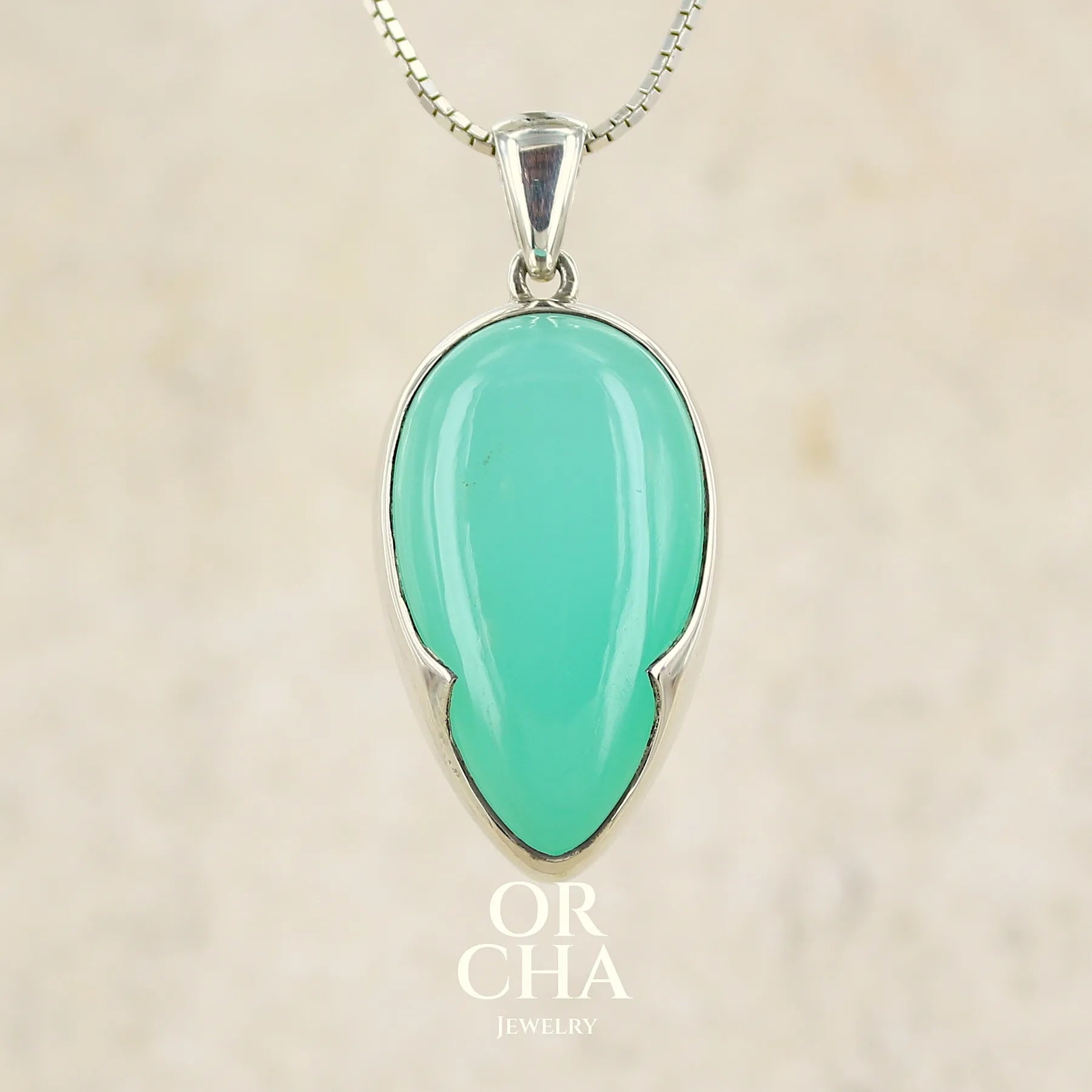 Pendentif pour femme en argent massif, sertie d'un cabochon de chrysoprase de couleur vert bleuté. Pierre de qualité translucide taillée en forme de goutte. Bijoux unique par Orcha jewelry
