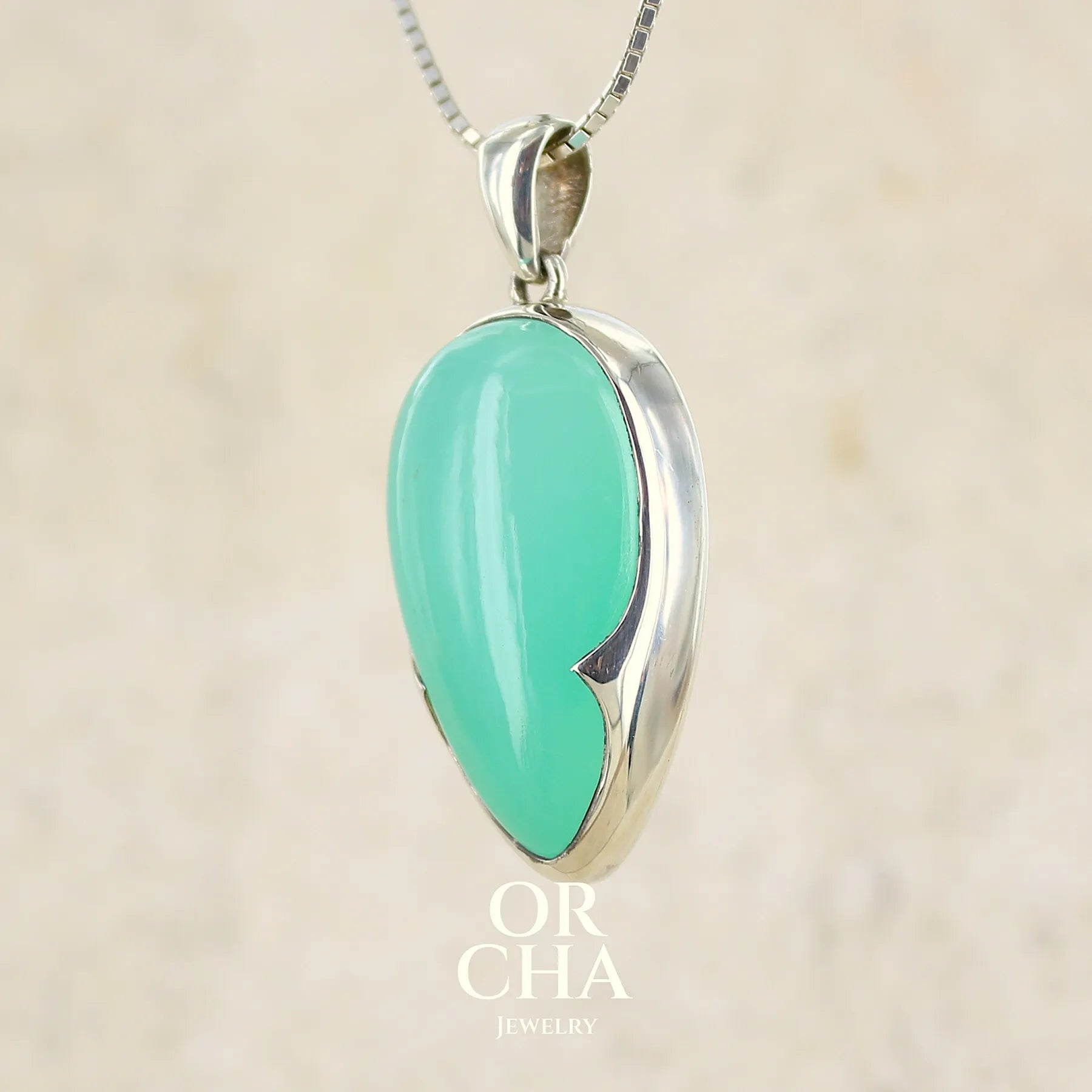 Pendentif pour femme en argent massif, sertie d'un cabochon de chrysoprase de couleur vert bleuté. Pierre de qualité translucide taillée en forme de goutte. Bijoux unique par Orcha jewelry