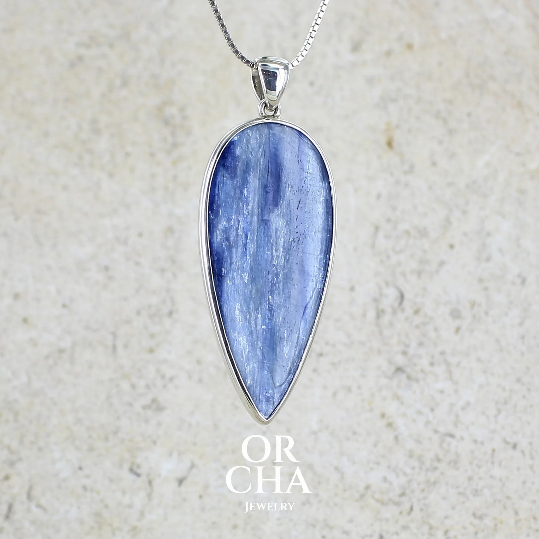 Pendentif en argent massif serti d'un cabochon de cyanite de couleur bleue jeans nacré. Pierre de qualité translucide taillée en forme de goutte inversée comportant des inclusions. Bijoux unique par Orchajewelry