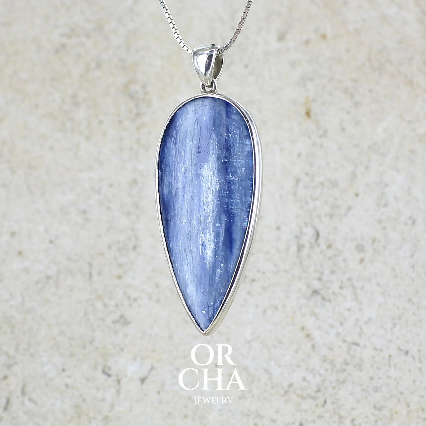 Pendentif en argent massif serti d'un cabochon de cyanite de couleur bleue jeans nacré. Pierre de qualité translucide taillée en forme de goutte inversée comportant des inclusions. Bijoux unique par Orchajewelry