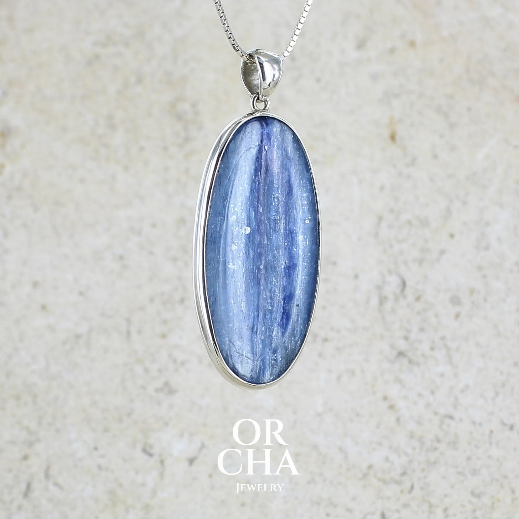 Pendentif en argent massif serti d'un cabochon ovale de cyanite de couleur bleue jeans nacré. Pierre de qualité translucide comportant des inclusions.Bijoux unique par Orcha Jewelry