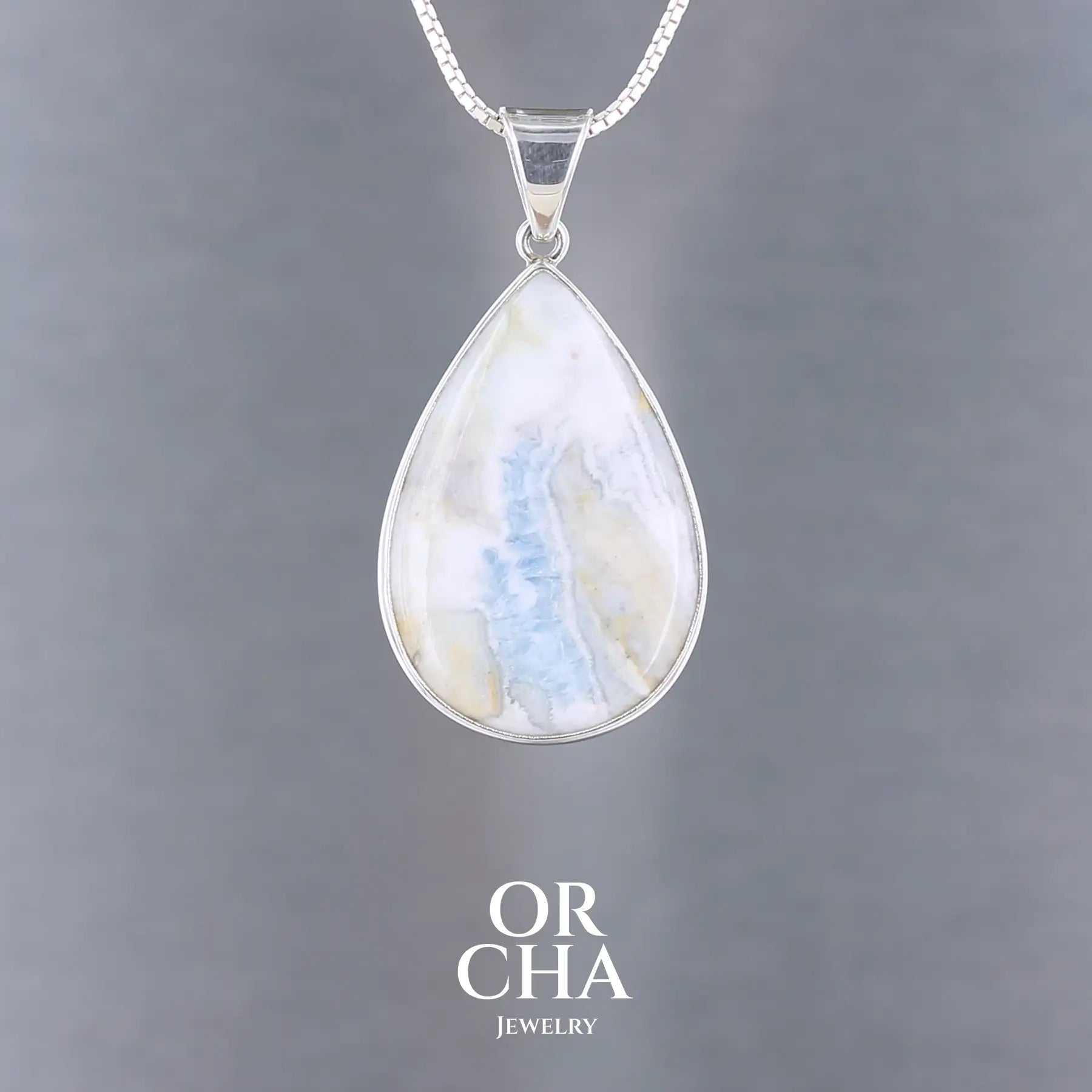 Pendentif pour femme en argent massif sertie d'une scheelite bleue. Pierre naturelle de couleur bleu, beige crème et blanc, de qualité opaque. Bijoux unique, éthique et durable présenté dans un coffret de notre marque, prêt à offrir. Livraison offerte, certificat d'authenticité, service client.
