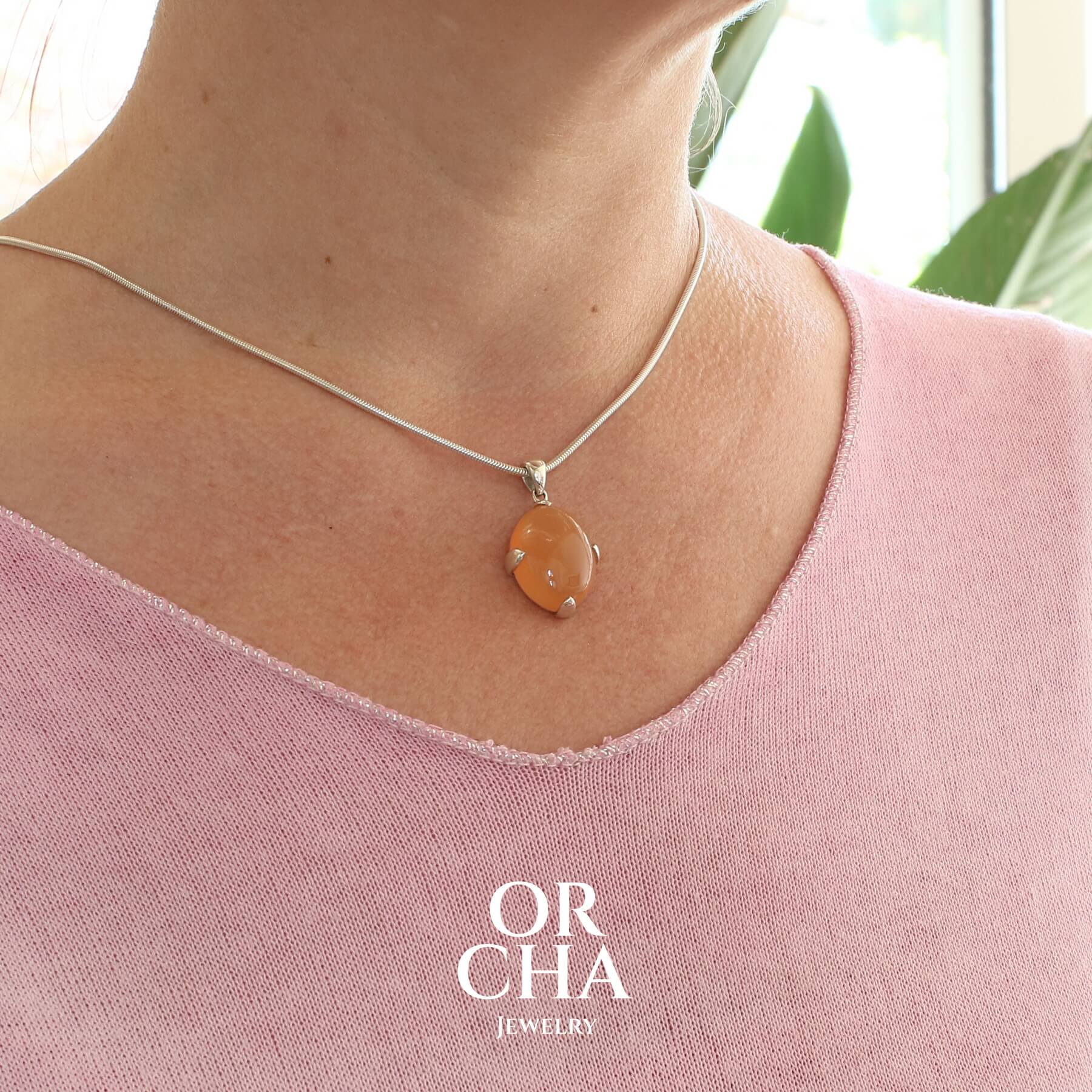 Pendentif pour femme en argent massif serti d'une pierre de lune orange. Pierre cabochon de forme ovale de couleur orange chatoyante à effet satiné. Bijoux unique, éthique et durable présenté dans un coffret de notre marque, prêt à offrir. Livraison offerte, certificat d'authenticité, service client.