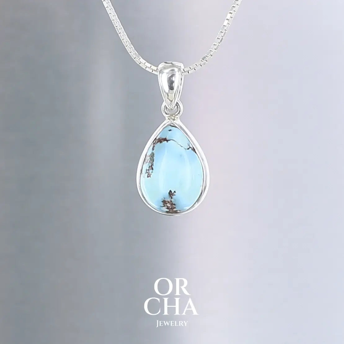 Élégant pendentif en forme de goutte présentant une turquoise Golden Hill d'un bleu ciel lumineux, parcourue de délicates veines minérales brunes caractéristiques. La pierre naturelle est sublimée par une fine monture en argent massif 925 qui épouse parfaitement ses contours. Cette création artisanale associe la sérénité du bleu turquoise à la pureté de l'argent, évoquant un fragment de ciel d'été. Un bijou intemporel aux les nuances naturelles.Livraison offerte, certificat d'authenticité, service client.