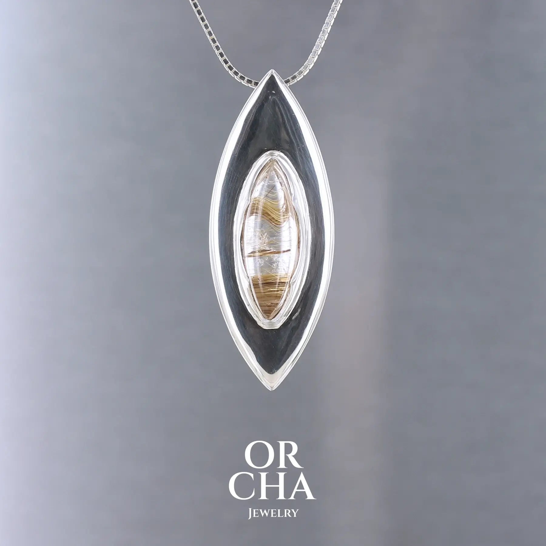 Pendentif en argent massif en forme d'amande, orné d'un quartz rutile doré naturel à inclusions filamenteuses, serti clos au centre d'une monture biseautée au design contemporain. Bijoux unique, éthique et durable présenté dans un coffret de notre marque, prêt à offrir. Livraison offerte, certificat d'authenticité, service client.