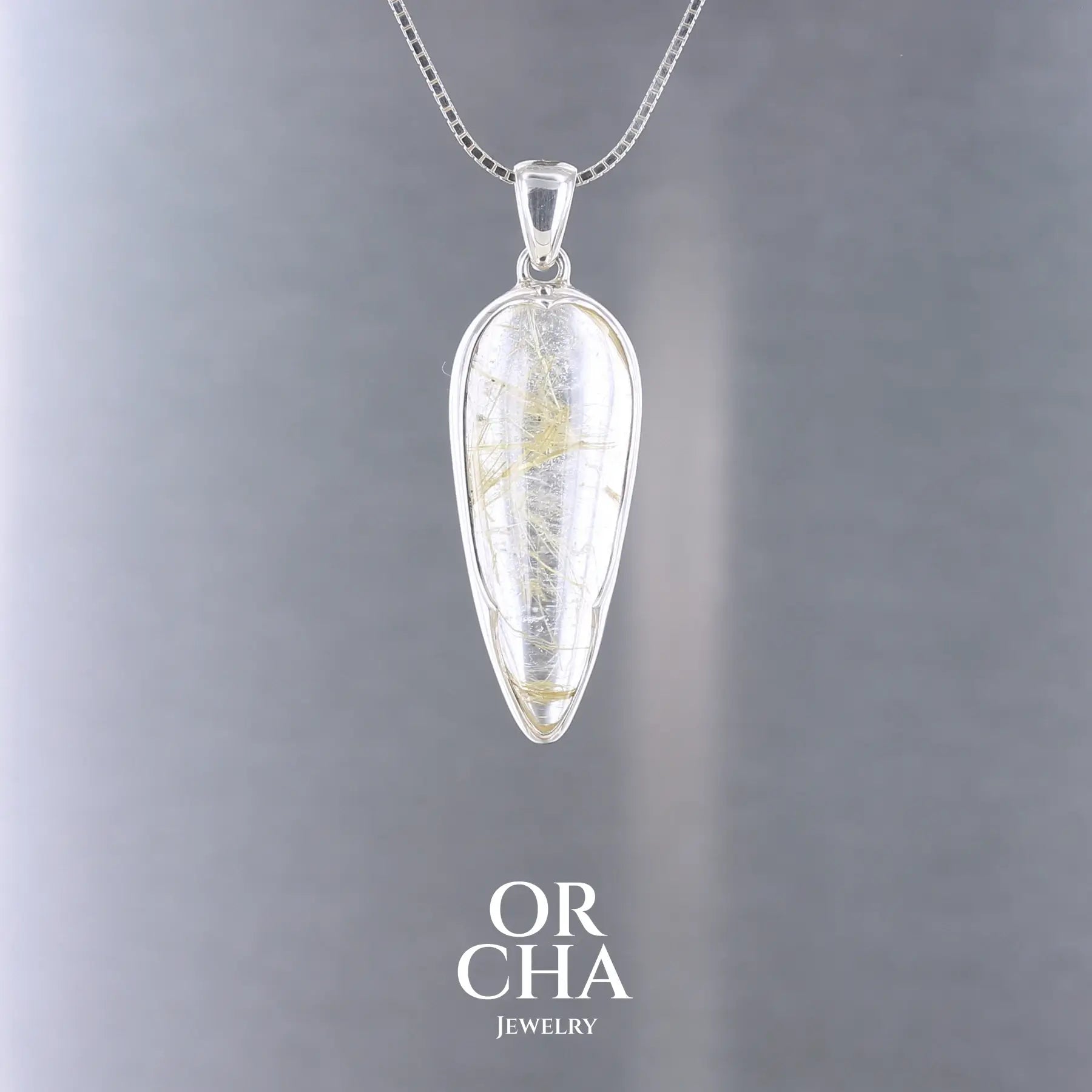 Pendentif en quartz rutile doré,en forme de goutte allongée, monté en argent massif 925 avec un serti clos à pointe.
Une création au design affirmé, sculptée pour révéler l’éclat des inclusions dorées qui parcourent la pierre comme une pluie figée de lumière. Bijoux unique, éthique et durable présenté dans un coffret de notre marque, prêt à offrir. Livraison offerte, certificat d'authenticité, service client.