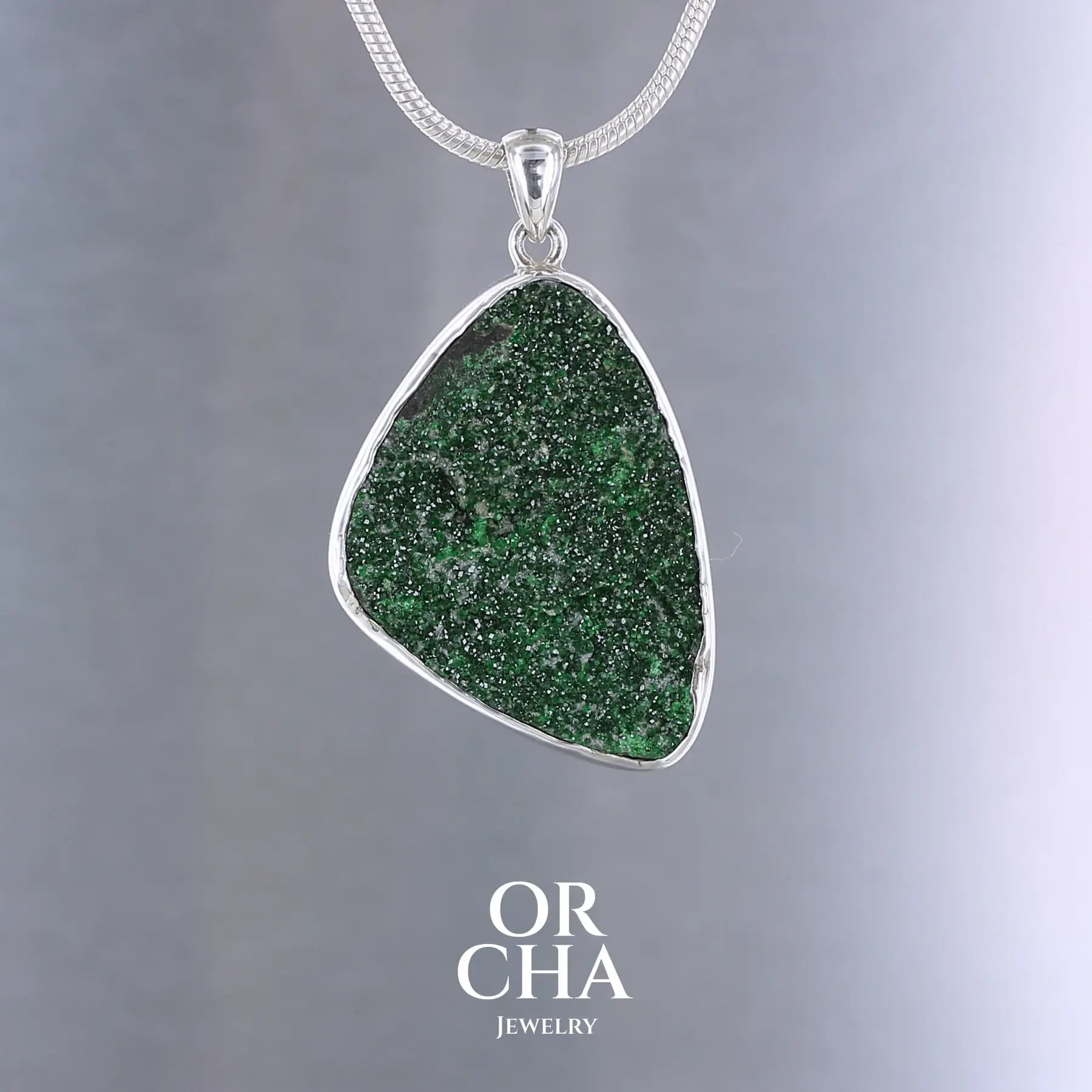 Pendentif en argent massif serti d'un grenat Uvarovite brute. Pierre naturelle recouverte de cristaux scintillants de couleur verte, taillée en forme de goutte. Bijoux unique, éthique et durable présenté dans un coffret de notre marque, prêt à offrir. Livraison offerte, certificat d'authenticité, service client.