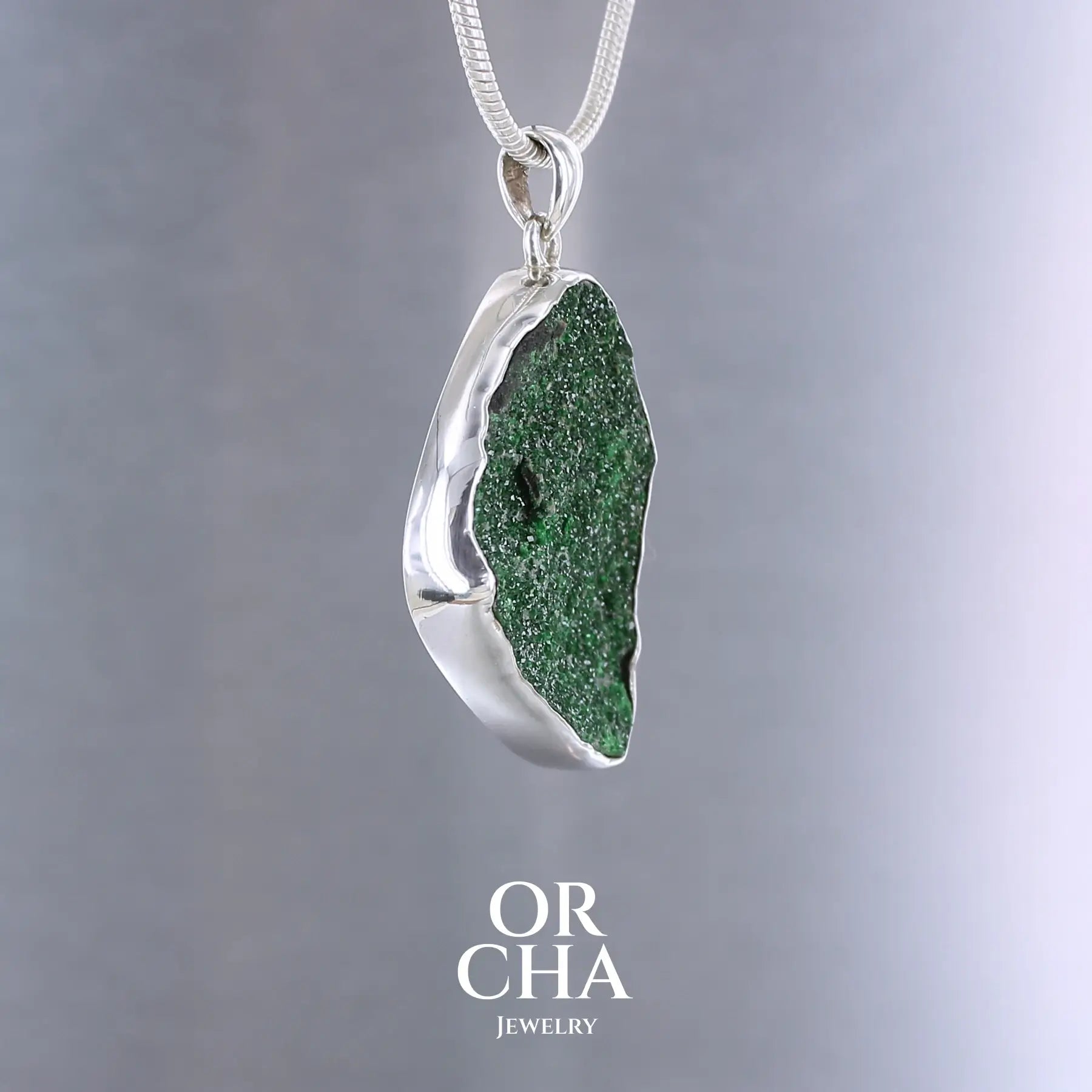 Pendentif en argent massif serti d'un grenat Uvarovite brute. Pierre naturelle recouverte de cristaux scintillants de couleur verte, taillée en forme de goutte. Bijoux unique, éthique et durable présenté dans un coffret de notre marque, prêt à offrir. Livraison offerte, certificat d'authenticité, service client.