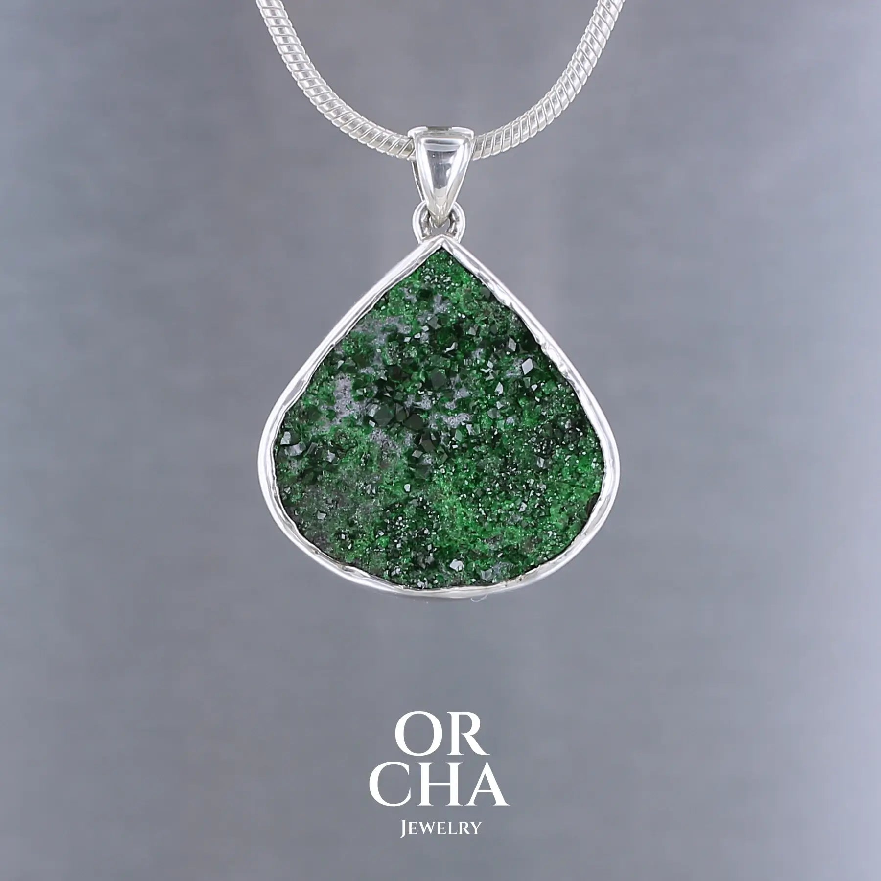 Pendentif en argent massif serti d'une Uvarovite brute ( variété de Grenat ). Pierre brute recouverte de cristaux scintillants de couleur verte, taillée en forme de goutte. Bijoux unique, éthique et durable présenté dans un coffret de notre marque, prêt à offrir. Livraison offerte, certificat d'authenticité, service client.
