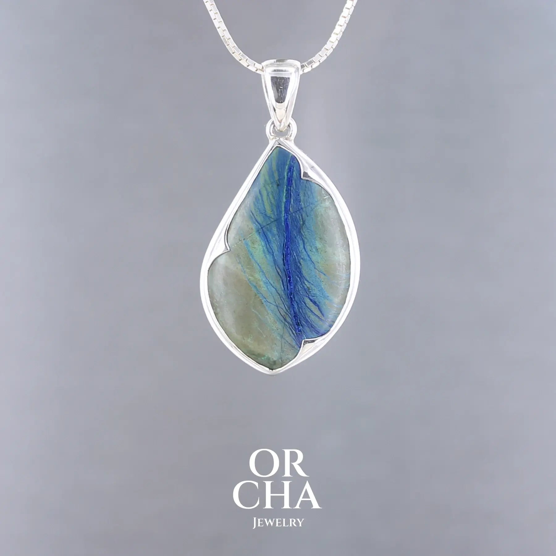 Pendentif azurite Morenci serti d'argent sterling 925. Pierre naturelle bleue profonde avec veines de malachite verte, forme ovale libre de 4 cm, sertissage clos argenté poli brillant. Bijoux unique, éthique et durable présenté dans un coffret de notre marque, prêt à offrir. Livraison offerte, certificat d'authenticité, service client.
