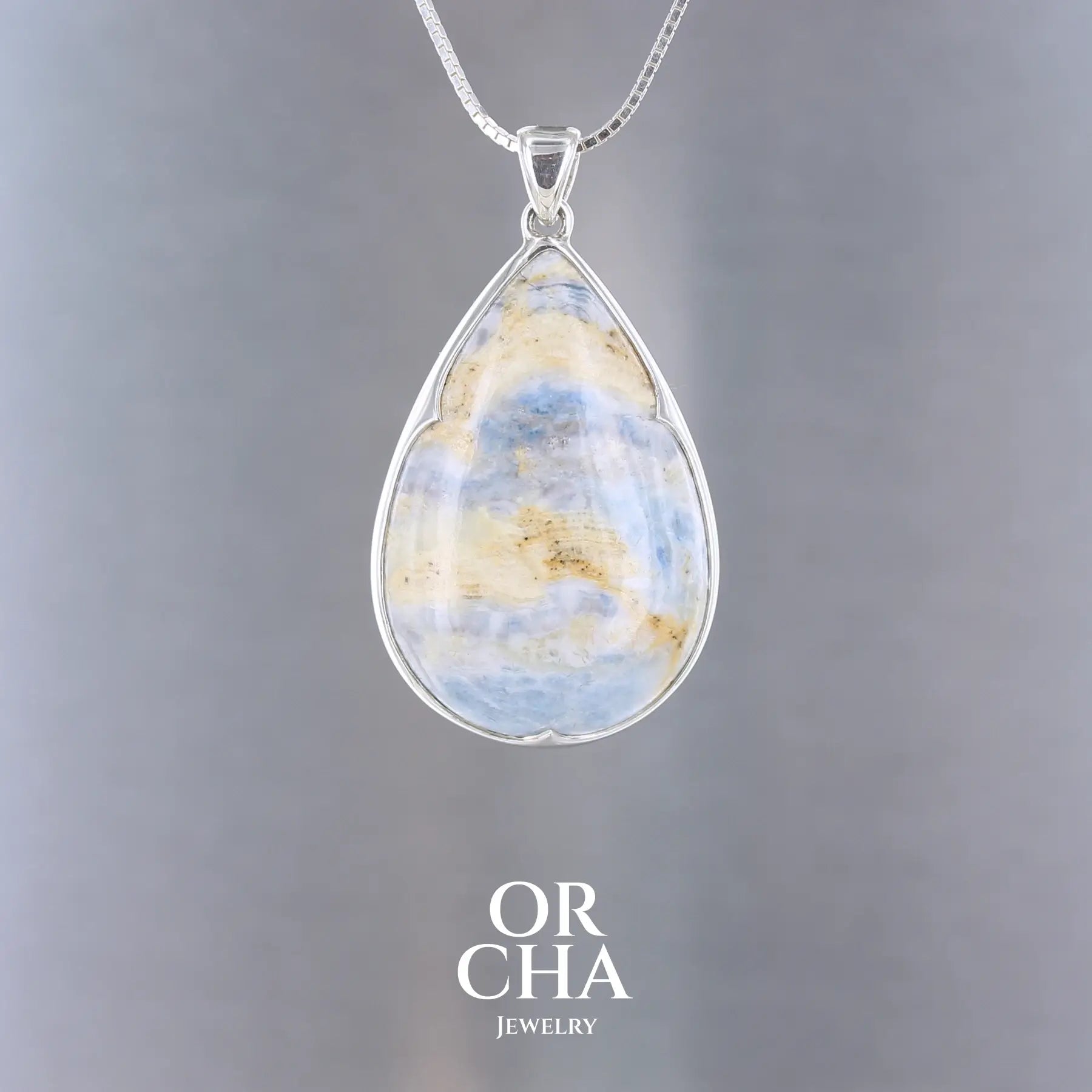 Pendentif pour femme en argent massif serti d'une Scheelite bleue. Pierre naturelle de couleur beige jaune et bleue ,taillée en cabochon en forme de goutte. Bijoux unique, éthique et durable présenté dans un coffret de notre marque, prêt à offrir. Livraison offerte, certificat d'authenticité, service client