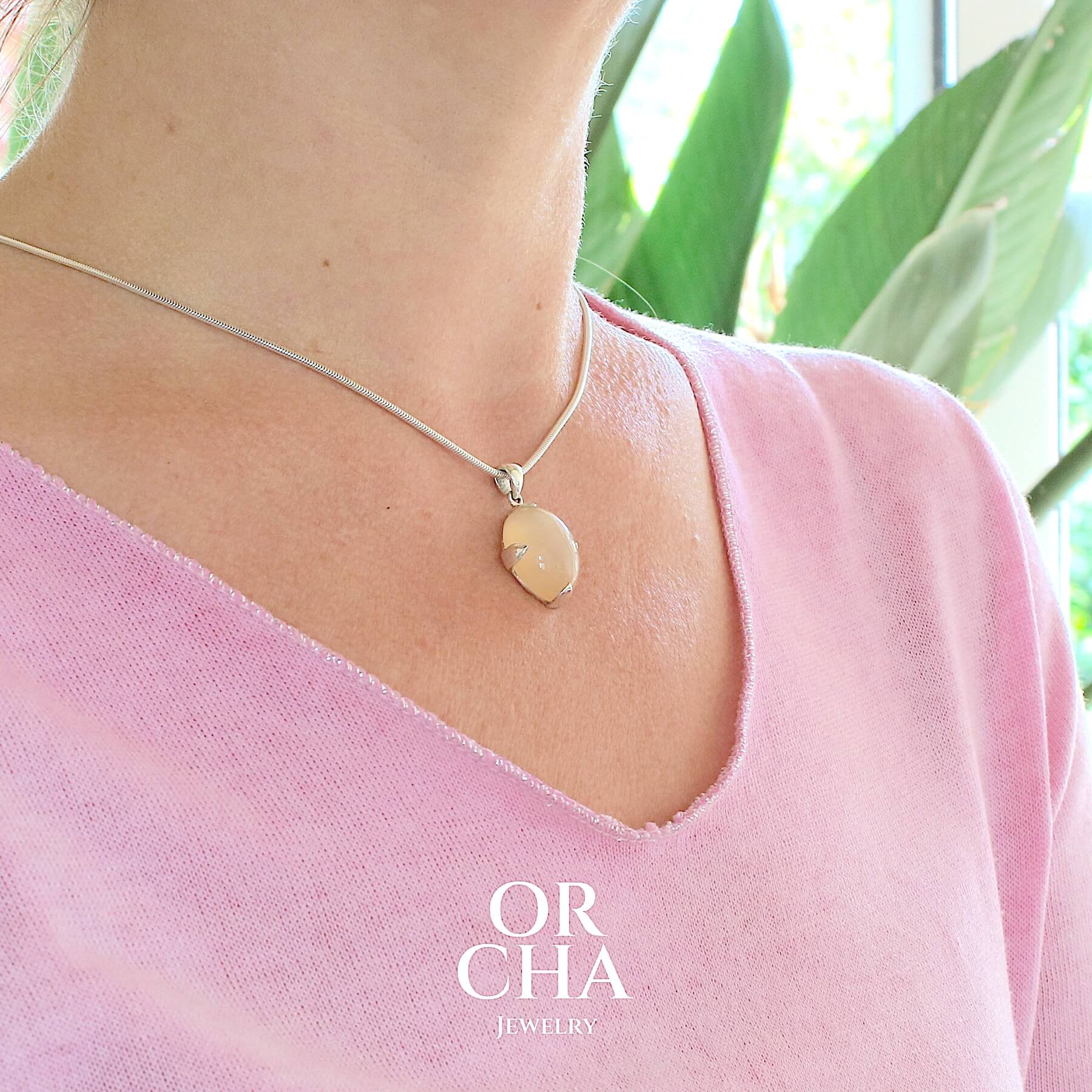 Pendentif pour femme en argent massif serti d'une pierre de lune orange clair, couleur chatoyante à effet satiné. Pierre naturelle taillée en cabochon de forme ovale serti de griffe. Bijoux unique, éthique et durable présenté dans un coffret de notre marque, prêt à offrir. Livraison offerte, certificat d'authenticité, service client