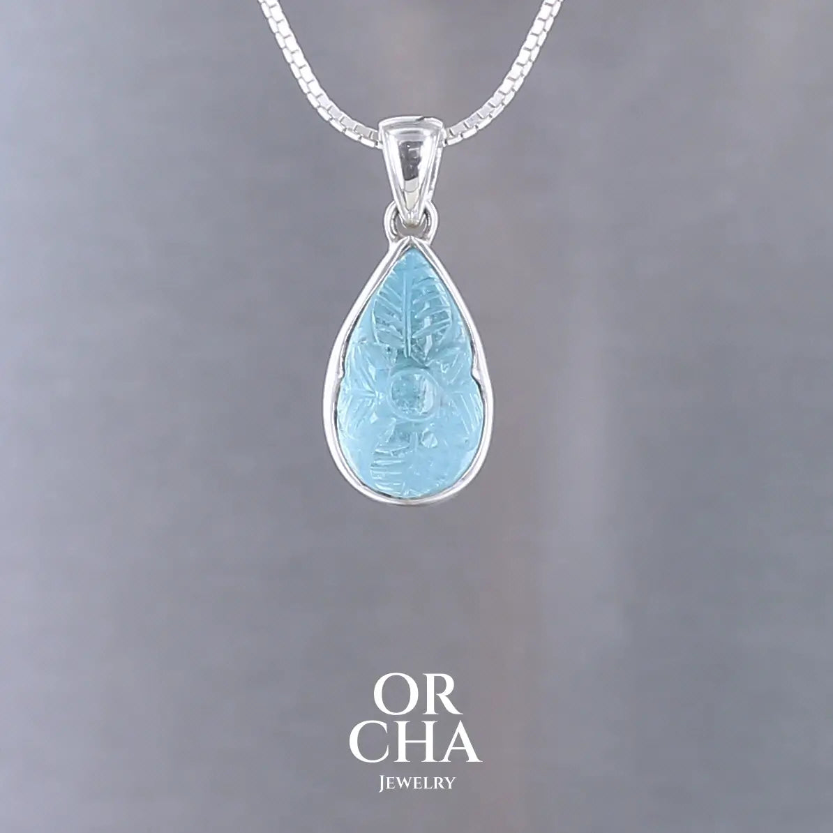 Pendentif pour femme en argent massif serti d'une topaze bleue sculptée de motifs floraux. Pierre cabochon en forme de goutte de couleur bleu ciel lumineux. Bijoux unique, éthique et durable présenté dans un coffret de notre marque, prêt à offrir. Livraison offerte, certificat d'authenticité, service client.