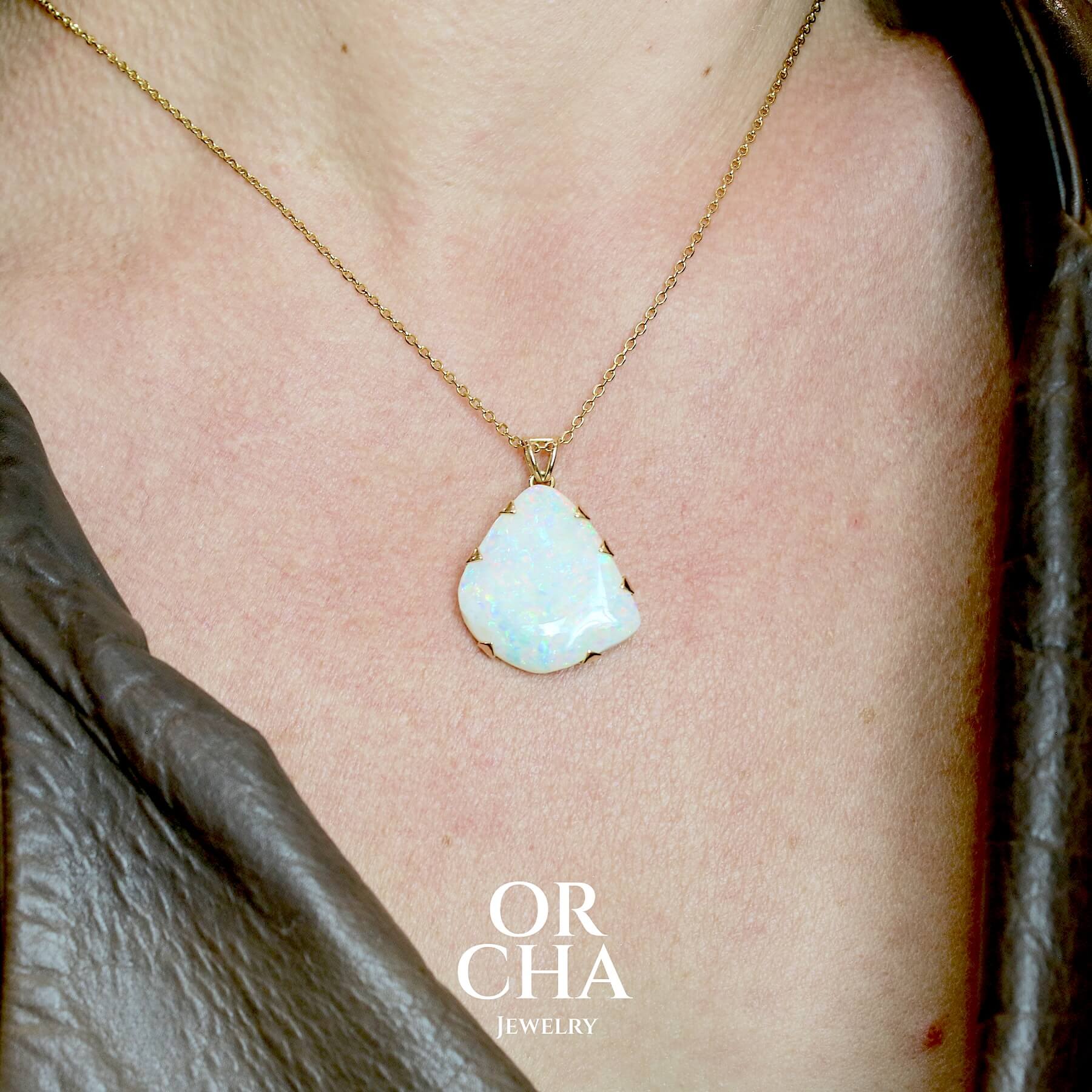 Pendentif pour femme en or jaune 18k serti d'une opale blanche de 17 carats aux feux multicolores. Pierre naturelle cabochon de forme irrégulière sertis  de griffes. A noter: présence de roche mère de couleur crème au dos de la pierre. Bijoux unique, éthique et durable présenté dans un coffret de notre marque, prêt à offrir. Livraison offerte, certificat d'authenticité, service client