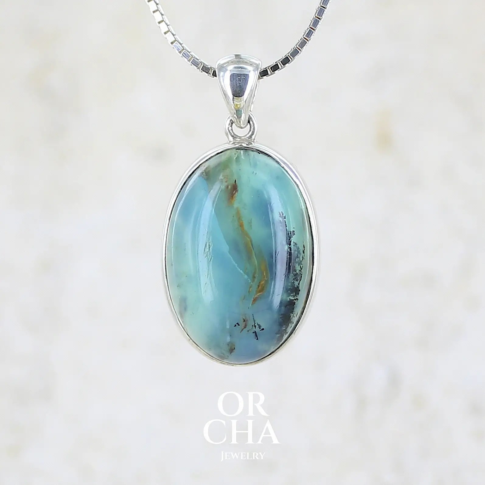 Pendentif en argent massif, sertie d'un cabochon ovale d'opale bleue du Pérou de couleur bleu laiteux foncé à inclusions de dendrites paysages noires et de roche mère marron. Pierre opaque et translucide. Bijoux unique, éthique et durable présenté dans un coffret de notre marque, prêt à offrir. Livraison offerte, certificat d'authenticité, service client.