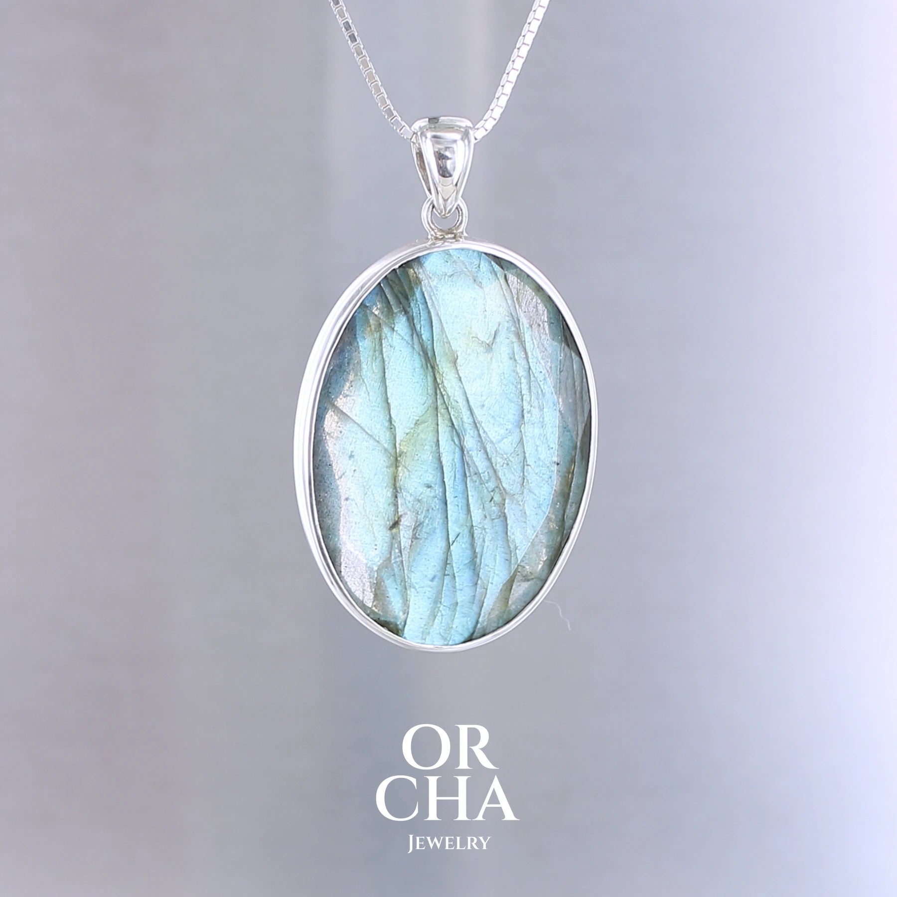 Pendentif ovale pour femme en argent massif serti d'une labradorite aux reflets bleus clairs, bleu vert selon la lumière. Pierre facettée naturelle translucide présentant des inclusions fréquents sur ce type de pierre. Bijoux unique, éthique et durable présenté dans un coffret de notre marque, prêt à offrir. Livraison offerte, certificat d'authenticité, service client.
