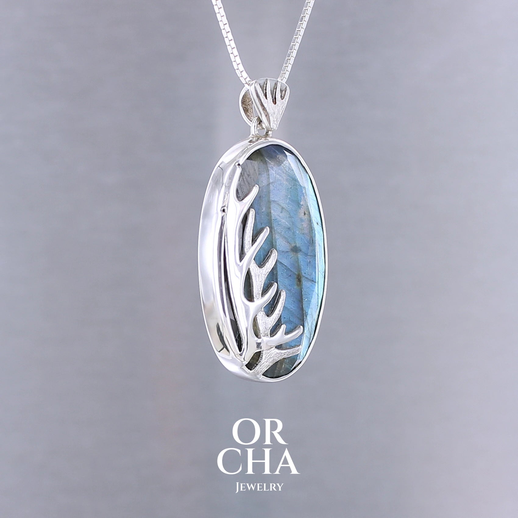 Pendentif pour femme en argent massif sertie d'une labradorite aux reflets bleus, Une ramure de cerf sculptée en argent penchasse la pierre. Pierre facettée naturelle translucide présentant des inclusions fréquents sur ce type de pierre. Bijoux unique, éthique et durable présenté dans un coffret de notre marque, prêt à offrir. Livraison offerte, certificat d'authenticité, service client.