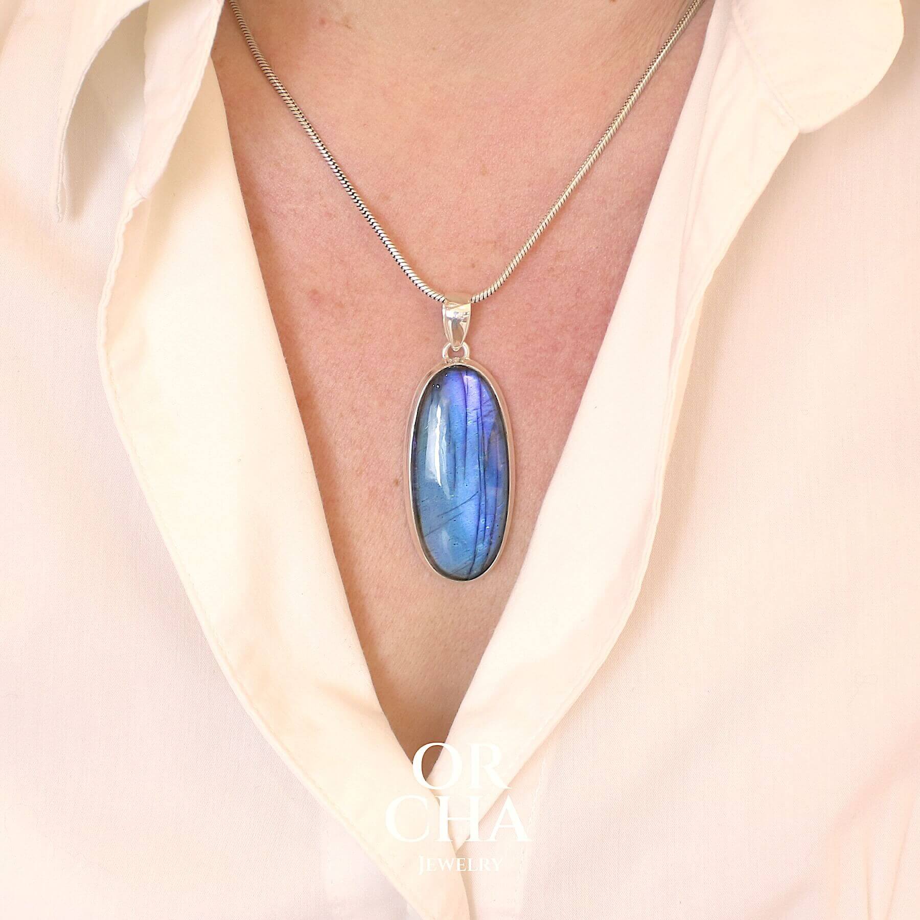Pendentif porté par une femme, bijou en argent massif sertie d'une labradorite aux reflets bleus nuits selon la lumière. Pierre cabochon naturelle translucide présentant des inclusions fréquents sur ce type de pierre. Bijoux unique, éthique et durable présenté dans un coffret de notre marque, prêt à offrir. Livraison offerte, certificat d'authenticité, service client.