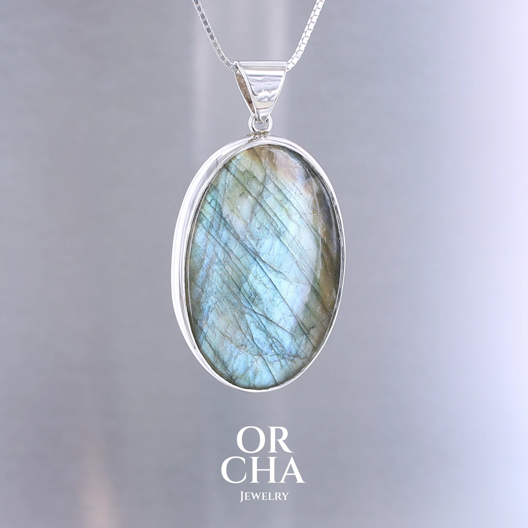 Pendentif pour femme en argent massif sertie d'une labradorite aux reflets bleu turquoise selon la lumière. Pierre cabochon naturelle translucide présentant des inclusions fréquents sur ce type de pierre. Bijoux unique, éthique et durable présenté dans un coffret de notre marque, prêt à offrir. Livraison offerte, certificat d'authenticité, service client.