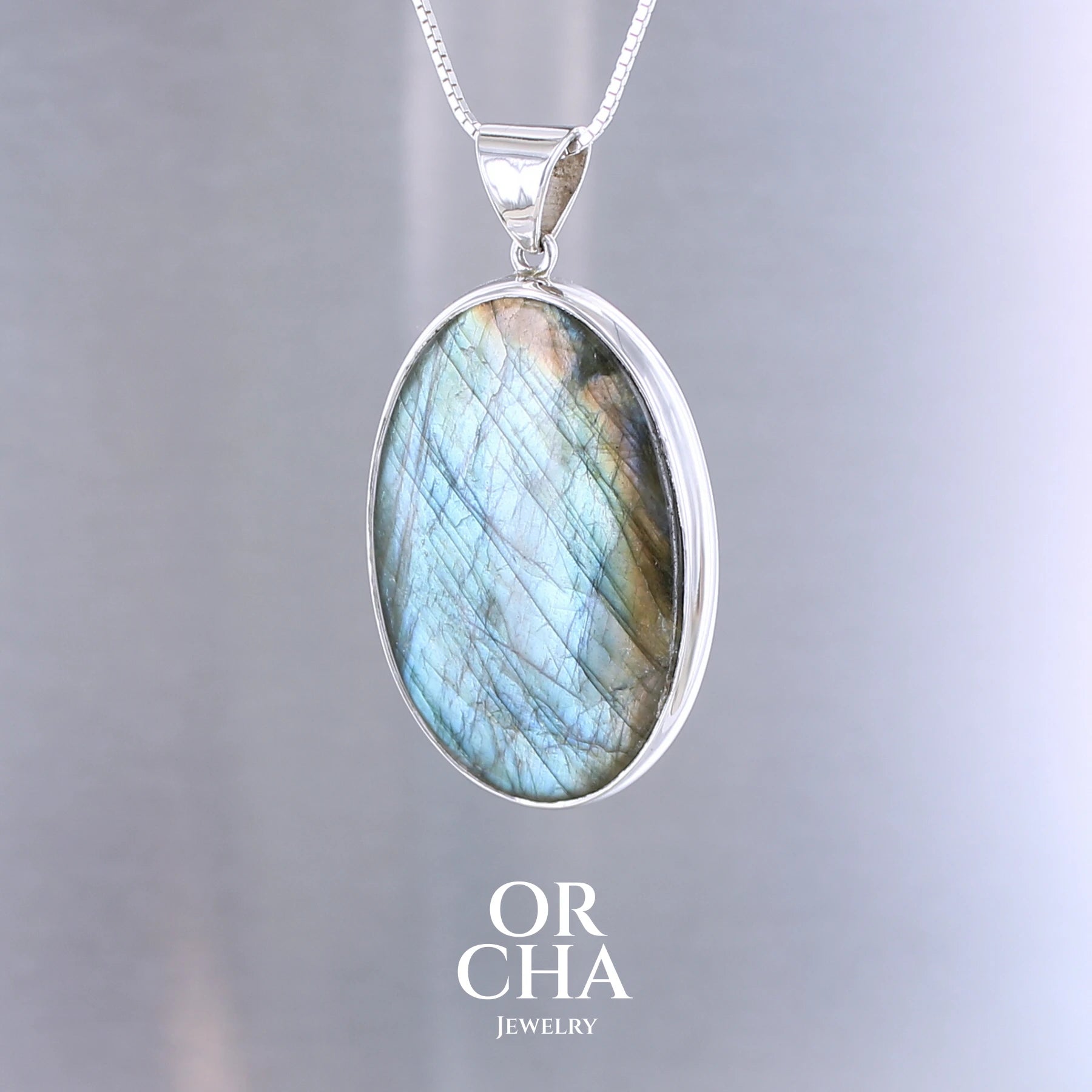 Pendentif pour femme en argent massif sertie d'une labradorite aux reflets bleu turquoise selon la lumière. Pierre cabochon naturelle translucide présentant des inclusions fréquents sur ce type de pierre. Bijoux unique, éthique et durable présenté dans un coffret de notre marque, prêt à offrir. Livraison offerte, certificat d'authenticité, service client.