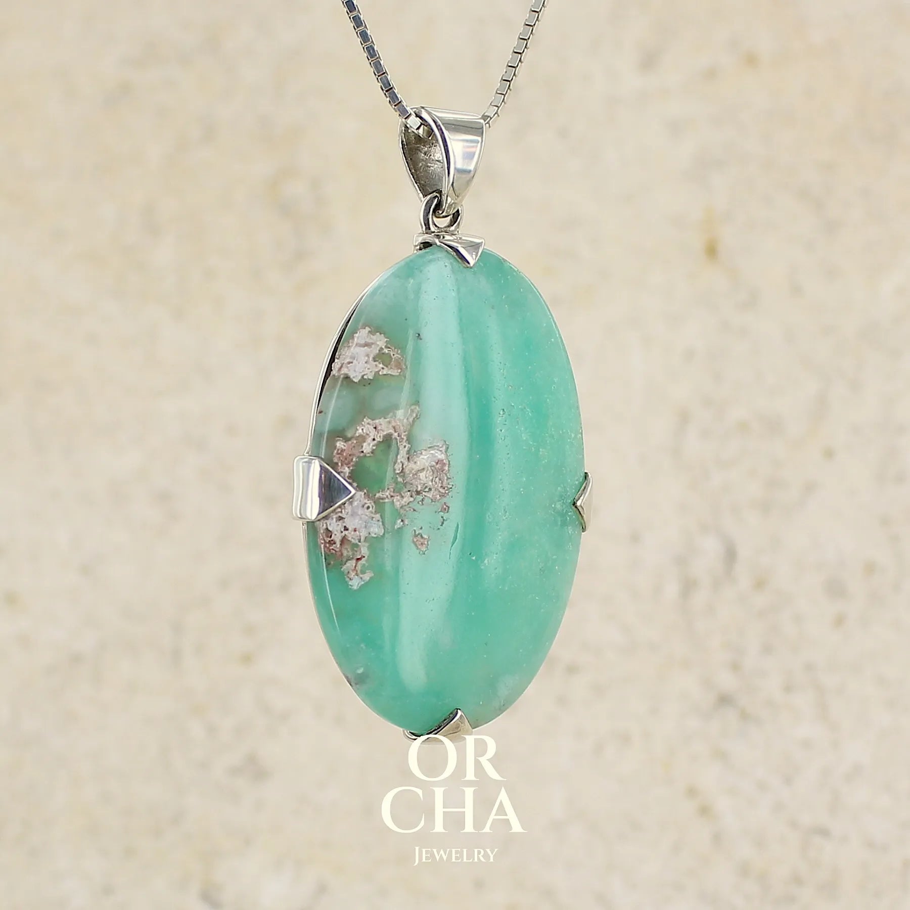 Pendentif ovale en argent massif, serti d'un cabochon de calcédoine de couleur bleue verte. Pierre de qualité translucide comportant des inclusions paysages blanches. Bijoux unique par Orcha Jewelry