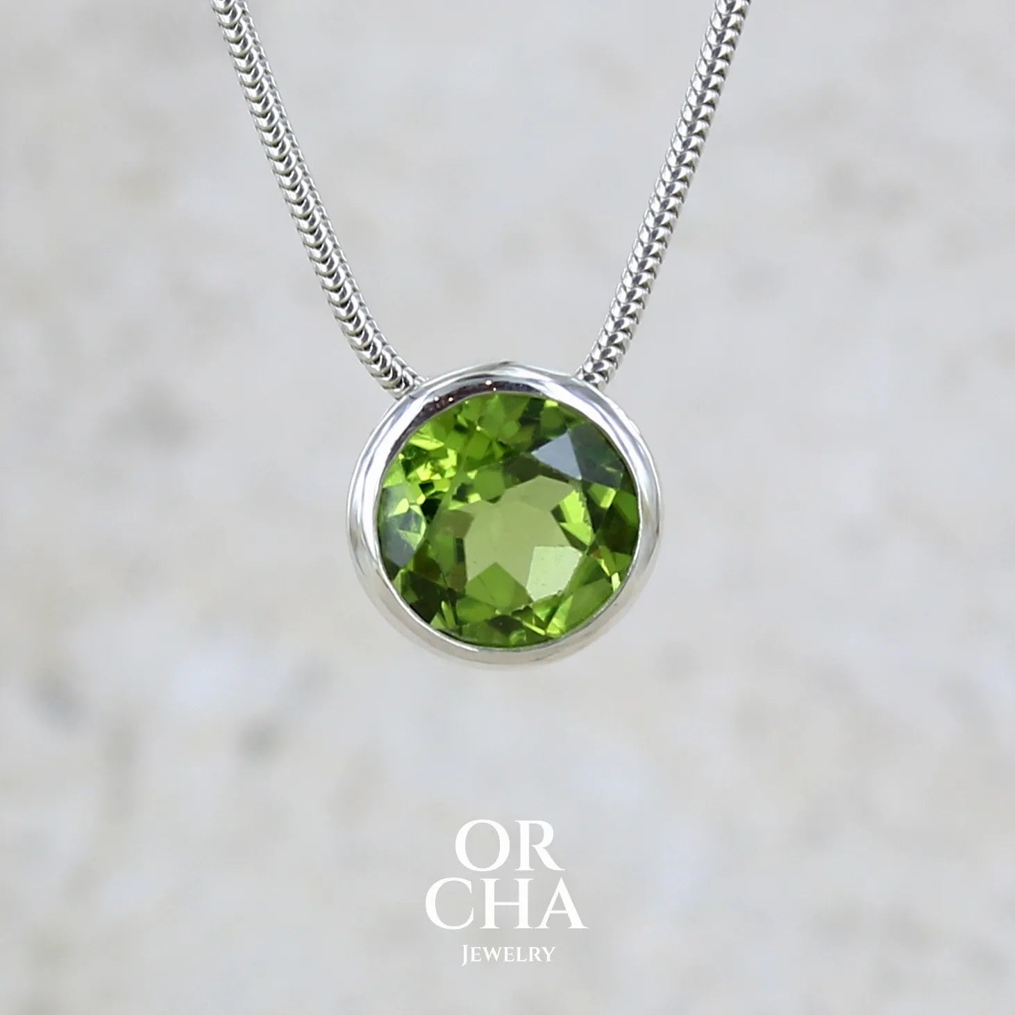 collier solitaire pour femme en argent massif serti d'un Péridot facettée de 4 carats. Pierre de forme ronde de qualité transparente, propre à l'oeil. Pierre naturelle de couleur vert olive doré intense et lumineuse. Pendentif monté sur une chaine en argent sterling de type maille serpent de 0,43 mm d'épaisseur et de 40 cm de longueur. Bijoux unique réalisé par Orchajewelry.