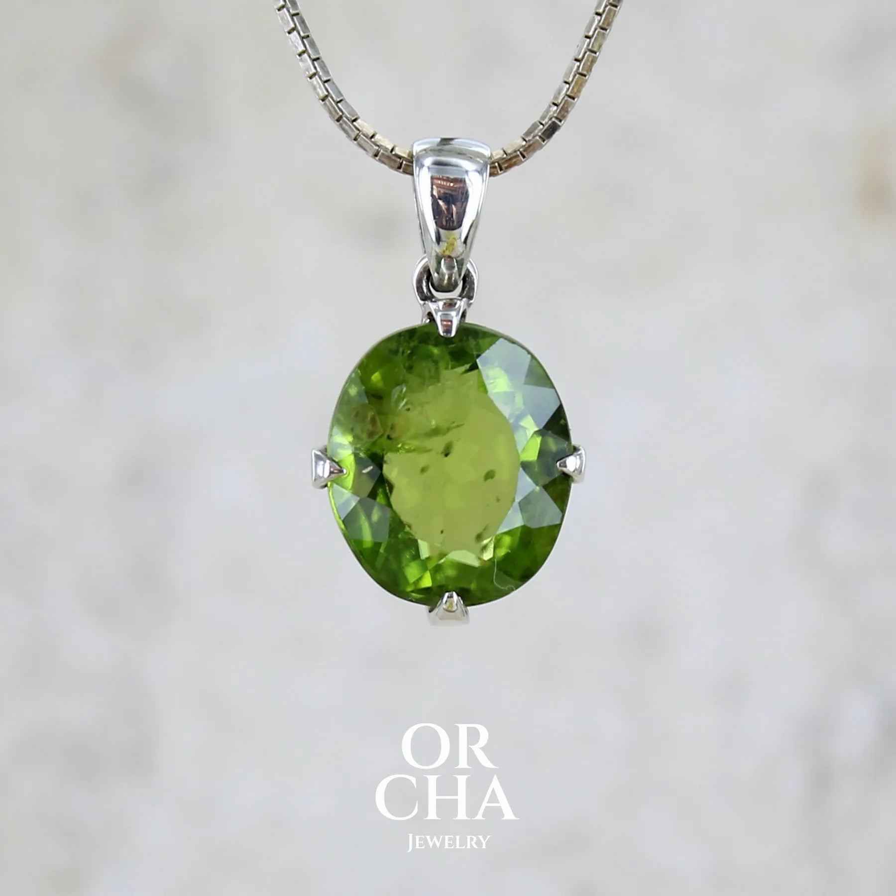 Pendentif pour femme en argent massif serti d'un péridot de couleur vert olive doré intense. Pierre taillée, de forme ovale, transparente présentant de nombreuse inclusions. Bijou unique réalisé par Orchajewelry
