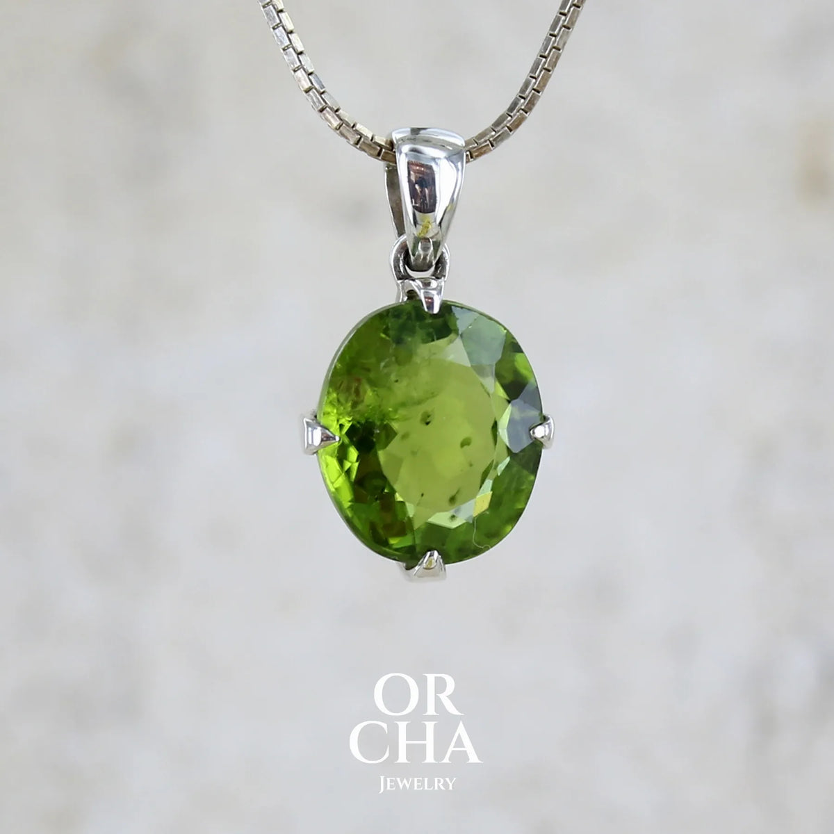 Pendentif pour femme en argent massif serti d'un péridot de couleur vert olive doré intense. Pierre taillée, de forme ovale, transparente présentant de nombreuse inclusions. Bijou unique réalisé par Orchajewelry