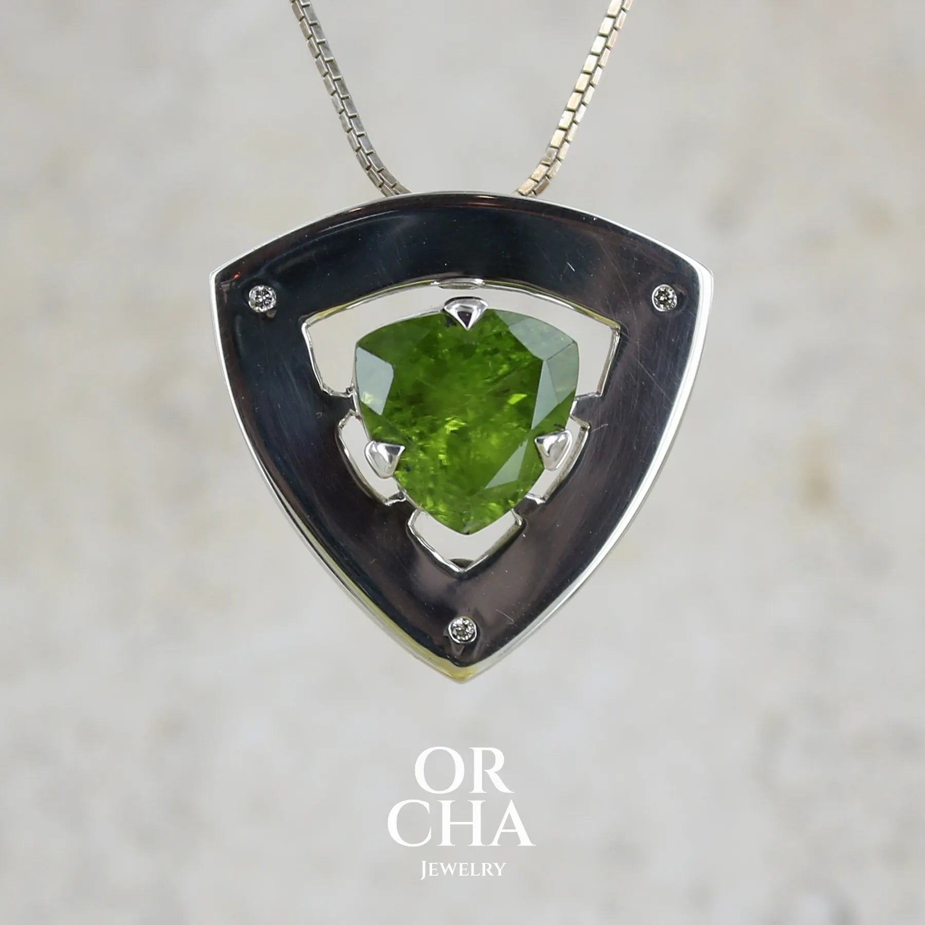 Pendentif contemporain pour femme en argent massif serti d'un péridot de couleur vert olive doré intense et de petits diamants. Pierre taillée, de forme triangulaire, transparente présentant de nombreuse inclusions. Bijou unique réalisé par Orchajewelry