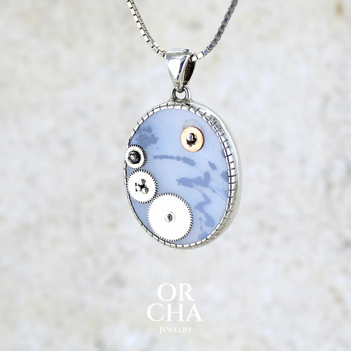Pendentif steam punk pour homme en argent massif sertie d'une tranche ovale d'agate dendritique de couleur gris et noir, orné de mécanismes de montre. Pierre translucide à inclusions de type tâches d'encre de dendrites de manganèse noires contrastées. Bijou unique réalisé par Orchajewelry