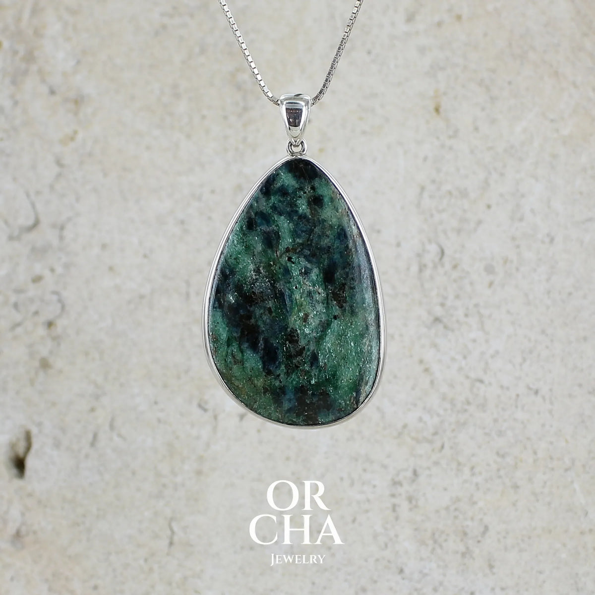 Pendentif pour femme en argent massif serti d'une pierre verte scintillante à inclusions bleutées et noires. Cabochon de forme libre de qualité opaque. Bijou unique réalisé par Orchajewelry