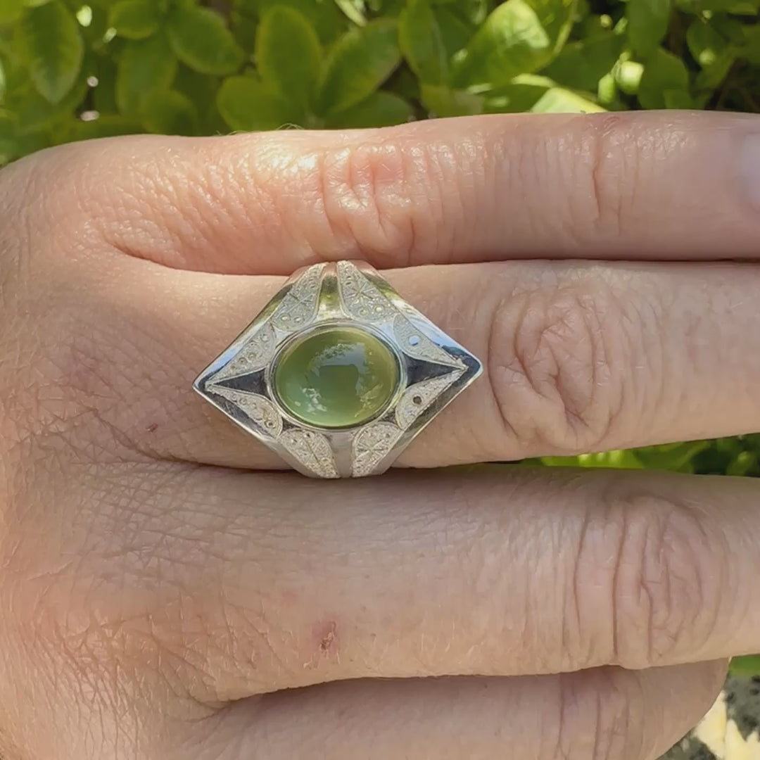Bague pour femme en argent massif sculptées d'étoiles et autres corps célestes sertie d'un cabochon ovale de préhnite de couleur verte pastel lumineuse. Pierre naturelle de qualité transparente présentant des inclusions. Bijoux unique réalisé en taille 54,5 par Orchajewelry.