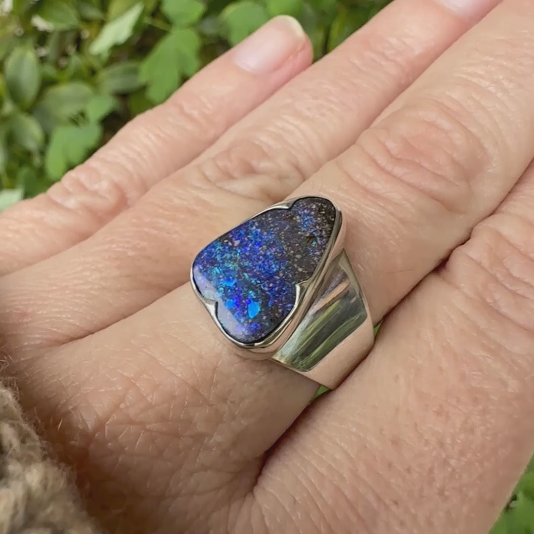 Bague pour femme en argent massif 925 sertie d'une opale boulder aux feux multicolores bleus violet et verts. Cabochon d'opale massive naturelle taillée en forme d'aile. Pierre de qualité opaque. Bijoux unique réalisé en taille 58 par Orcha Jewelry.