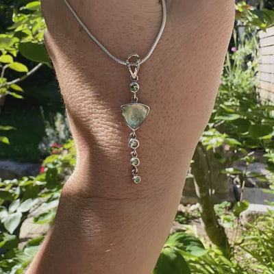 Pendentif pour femme en argent massif sertie d'un cabochon triangulaire de Préhnite ainsi que de petites tourmalines vertes formant une cascade colorée vert pastel lumineux. Pierre transparente à inclusions. Bijou unique réalisé par Orchajewelry