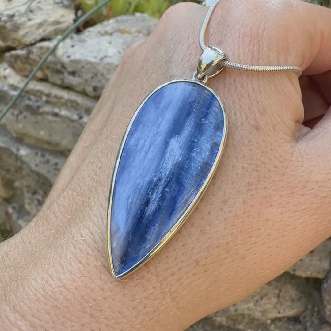 Pendentif en argent massif serti d'un cabochon de cyanite de couleur bleue jeans nacré. Pierre de qualité translucide taillée en forme de goutte inversée comportant des inclusions. Bijoux unique par Orchajewelry