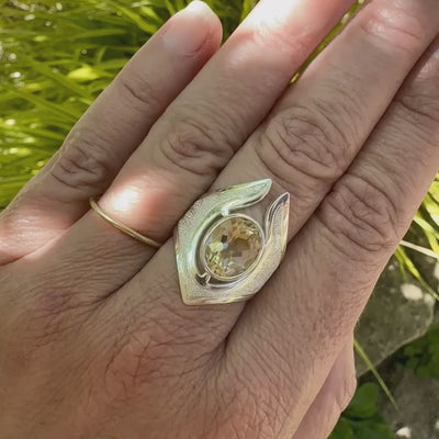 vidéo d'une main qui porte une grande bague contemporaine pour femme en argent massif sertie d'une Citrine. Pierre facettée de forme ovale de qualité transparente, propre à l'oeil. Pierre naturelle de couleur jaune doré lumineux. Bijoux unique, éthique et durable présenté dans un coffret de notre marque, prêt à offrir. Livraison offerte, certificat d'authenticité, service client.
