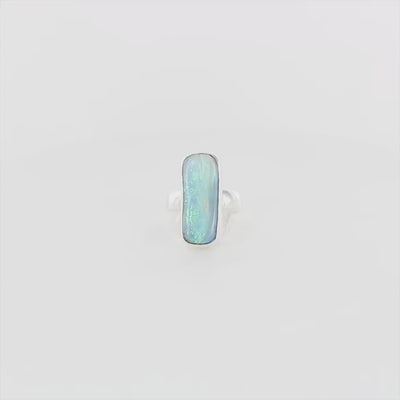 Bague en argent massif, avec une grande opale boulder rectangulaire sertie en cabochon. La pierre présente des reflets irisés bleu-vert intenses, ponctués de touches orangées. Le métal est lisse et poli, avec un anneau droit, épais et solide. Bague réalisée en taille 60. Bijoux unique, éthique et durable présenté dans un coffret de notre marque, prêt à offrir. Livraison offerte, certificat d'authenticité, service client.