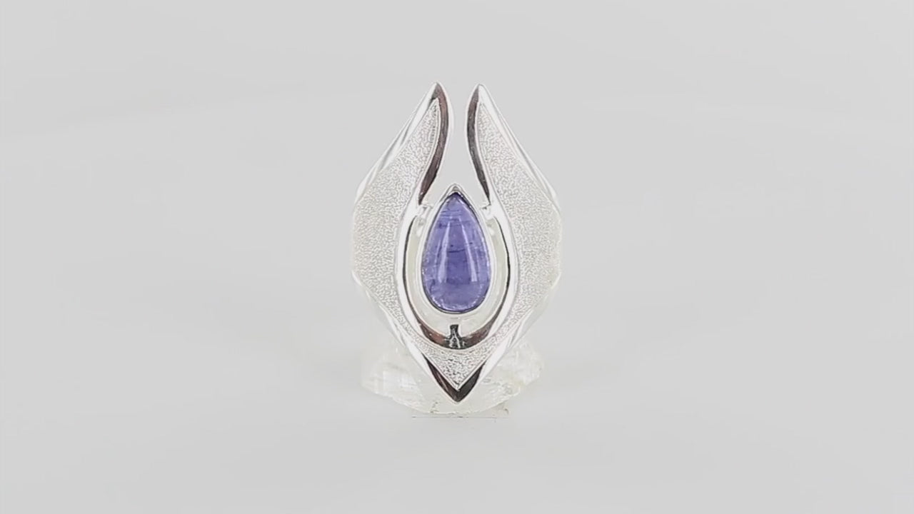 Bague de créateur en argent massif pour femme sertie d'une Tanzanite. Pierre cabochon en forme de goutte de qualité transparente avec inclusions. Pierre naturelle de couleur bleu lavande. Bague réalisée en taille 56. Bijoux unique, éthique et durable présenté dans un coffret de notre marque, prêt à offrir. Livraison offerte, certificat d'authenticité, service client.