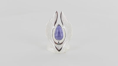 Bague de créateur en argent massif pour femme sertie d'une Tanzanite. Pierre cabochon en forme de goutte de qualité transparente avec inclusions. Pierre naturelle de couleur bleu lavande. Bague réalisée en taille 56. Bijoux unique, éthique et durable présenté dans un coffret de notre marque, prêt à offrir. Livraison offerte, certificat d'authenticité, service client.