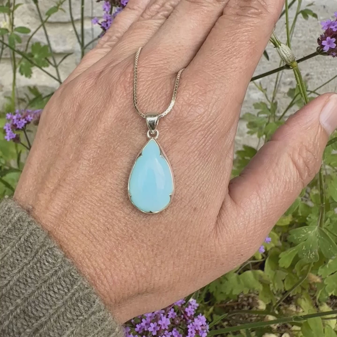 photo sur model d'un pendentif pour femme en argent massif, sertie d'un cabochon d'opale bleue du Pérou de couleur bleu ciel clair. Pierre en forme de goutte. Pierre opaque. Bijoux unique, éthique et durable présenté dans un coffret de notre marque, prêt à offrir. Livraison offerte, certificat d'authenticité, service client.