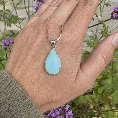 photo sur model d'un pendentif pour femme en argent massif, sertie d'un cabochon d'opale bleue du Pérou de couleur bleu ciel clair. Pierre en forme de goutte. Pierre opaque. Bijoux unique, éthique et durable présenté dans un coffret de notre marque, prêt à offrir. Livraison offerte, certificat d'authenticité, service client.