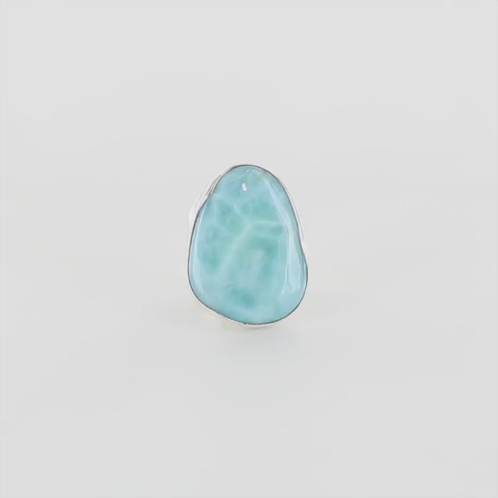 Bague artisanale en argent sterling 925 sertie d'une pierre naturelle de larimar bleu intense de République Dominicaine. La gemme ovale présente des nuances bleu caraïbe profondes avec des veines blanches nacrées rappelant les vagues océaniques. Sertissage clos en argent massif épousant parfaitement les contours naturels de la pierre.  Taille 60. Bijoux unique, éthique et durable présenté dans un coffret de notre marque, prêt à offrir. Livraison offerte, certificat d'authenticité, service client.