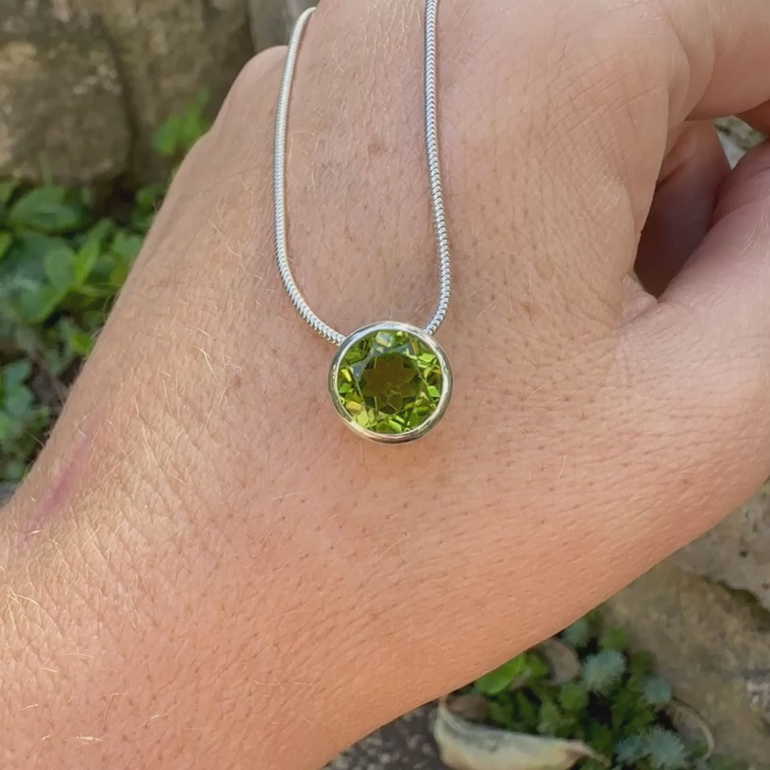 collier solitaire pour femme en argent massif serti d'un Péridot facettée de 4 carats. Pierre de forme ronde de qualité transparente, propre à l'oeil. Pierre naturelle de couleur vert olive doré intense et lumineuse. Pendentif monté sur une chaine en argent sterling de type maille serpent de 0,43 mm d'épaisseur et de 40 cm de longueur. Bijoux unique réalisé par Orchajewelry.